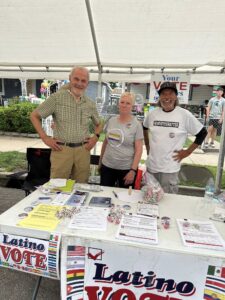 Three volunteers stand behind a table, which has flyers and other voting information.
